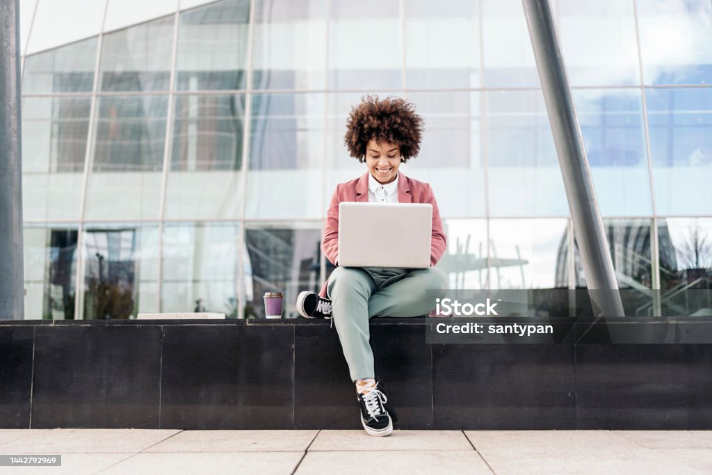 Business Woman Using Laptop Outdoors Business woman with afro hair wearing formal clothes sitting outdoors in business area and using her computer. People Stock Photo