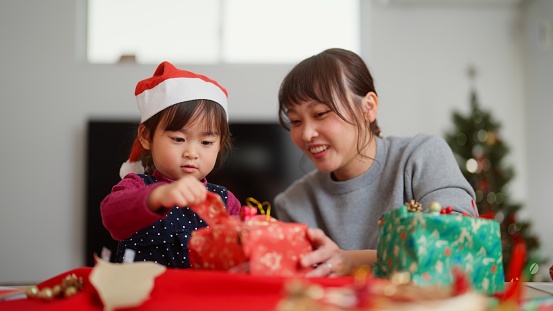 A mother and her small preschool age daughter are opening Christmas presents in the living room at home.