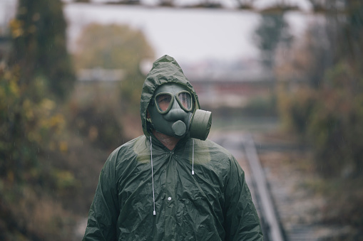 Man wearing gas mask and protective clothes wandering on old railroads