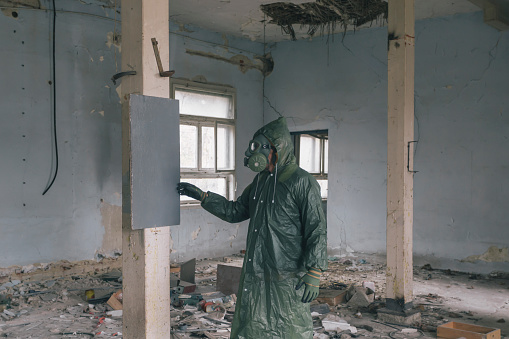 Man wearing gas mask and protective clothes at ruined abandoned building