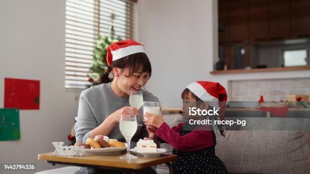 母親と小さな就学前の娘は、自宅のリビングルームのソファに座ってリラックスしながら、クリスマスケーキを食べたり飲み物を飲んだりしています