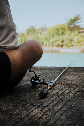 A person who only looks at his knees is sitting with a fishing rod