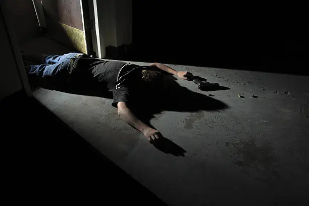 A body lying on a warehouse floor in a doorway with a hand gun and spent shells lying next to him.