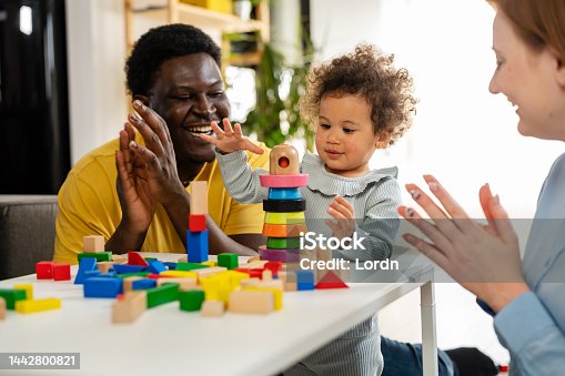 istock Mother and father supporting their cute little daughter in playing with colorful didactic wooden toys at home 1442800821