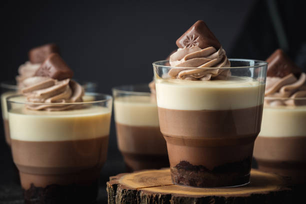 istock Layered dessert Trifles in a transparent glass.  Sponge biscuit and three chocolate mousse layers. Chocolate souffle trifle cake in individual disposable transparent cups. Black background 1442804441