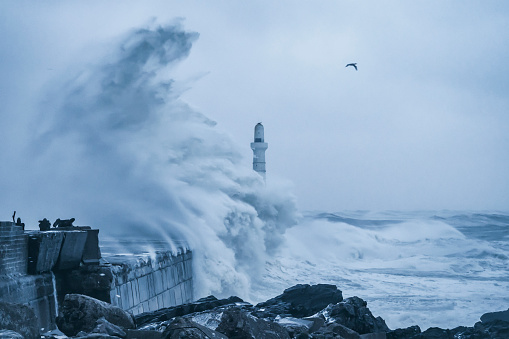 Waves from stormy weather in the north sea breaking against the wall at the entrance to Aberdeen Harbour, Scotland.