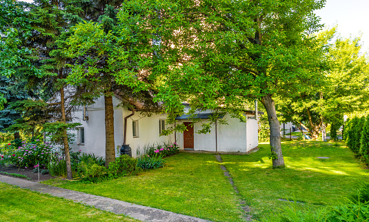 Warsaw, Poland - June 26, 2022: Vintage village house and yard at Zdziechowskiego street squeezed between new office buildings in highly developed Industrial Sluzewiec quarter of Mokotow district of Warsaw