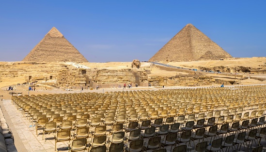 Giza, Egypt, April 15, 2022: View of the auditorium in the Giza Necropolis. In the background are the Pyramid of Khafre (left, known also as Pyramid of Chephren) and Pyramid of Cheops. In the middle is the Great Sphinx. The pyramid field of Giza is listed as UNESCO World Heritage Site.
