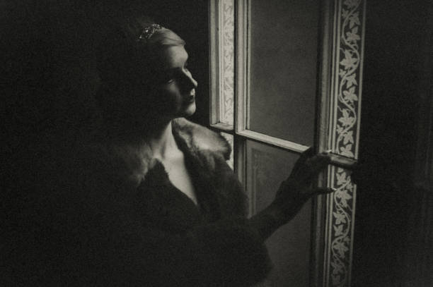 Portrait of a woman in evening dress. She stands at a window of the staircase at night. She is illuminated only by light from a street lamp. She is smoldering in memories.