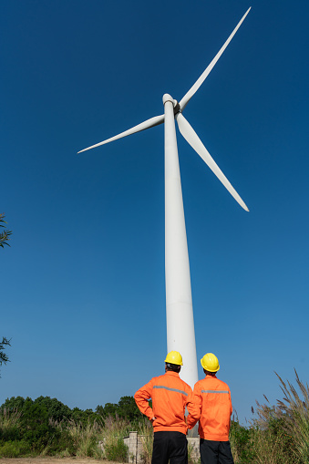 Two electrical engineers shaking hands celebrating completion of work under windmill