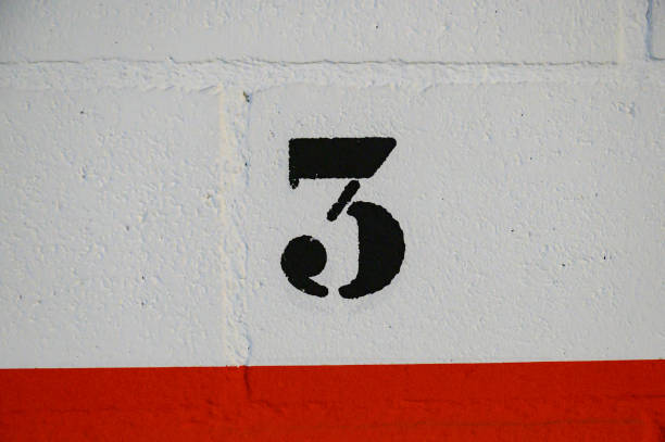 istock Number 3 three painted in black with a stencil and spray paint on a white block wall in a garage, below a strip of red line 1442820521