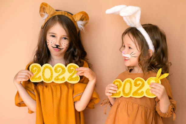грустная девочка с номером 2022 в облике тигра и ребенок с номером 2023 нового года наряжаются в зайчика. - face paint child paint rabbit стоковые фото и изображения