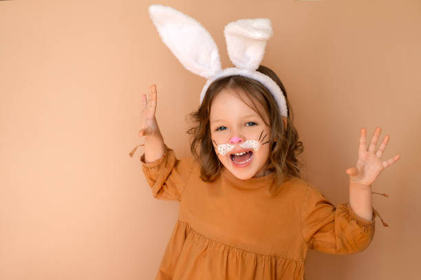 веселая смеющаяся девушка с ушами и лицом, раскрашенным акварелью в образе кролика. кролик – символ восточного календаря 2023 года - face paint child paint rabbit стоковые фото и изображения