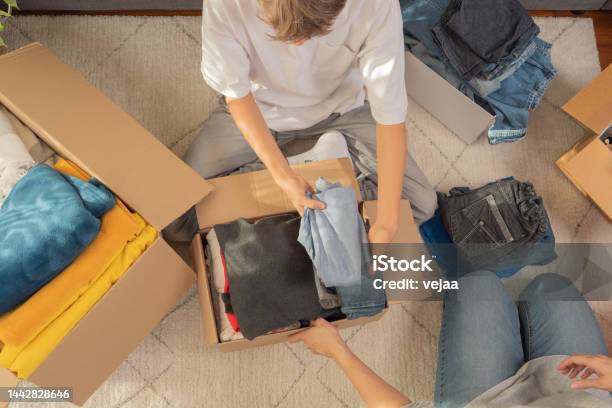 Woman And Child Sorting Clothes And Packing Into Cardboard Box Donations For Charity Help Low Income Families Declutter Home Sell Online Moving Moving Into New Home Recycling Sustainable Living Stock Photo - Download Image Now
