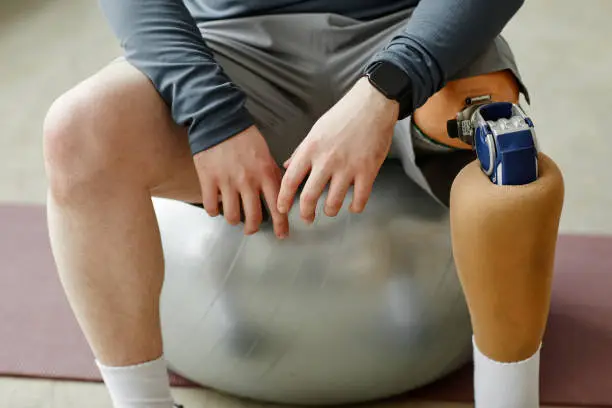 Close up of man with prosthetic leg sitting on fitness ball during home workout