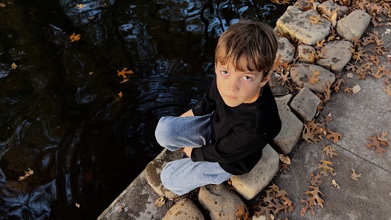 Caucasian Serious Little boy playing with water at a pond looking at the camera