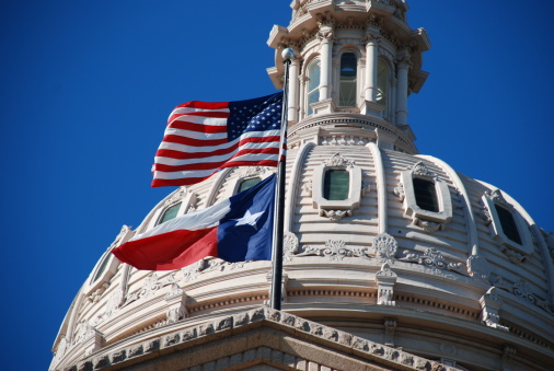 closer look of the Texas state capitol building's dome with waving flags of the United States and Texas