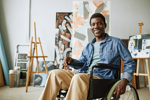 Young successful painter in casualwear sitting in wheelchair in front of camera while spending time in studio of arts at leisure