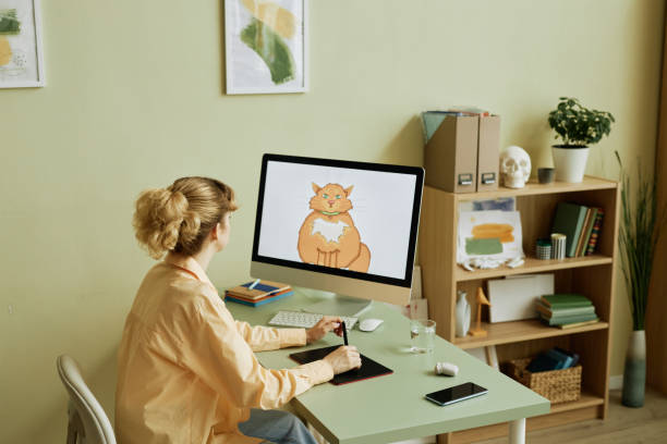 istock Desktop computer with fat ginger cat drawn by girl on screen 1442832671