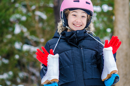 Headshot of teenage girl with ski helmet holding ice skates during winter day