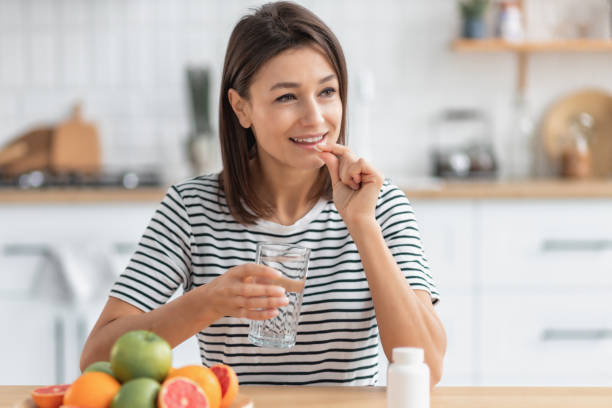 Healthy lifestyle. Happy caucasian woman holding nutritional supplement capsule or painkiller and glass of water, smiling friendly stock photo