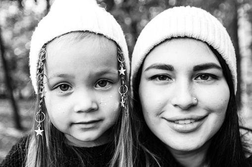Mom and little daughter. Close up of faces. Tenderness of mother and daughter. Summer park. Green trees. The concept of a young family. Black and white photography.