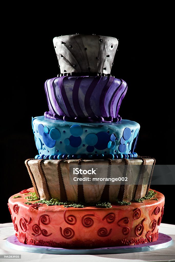 Super cool wedding cake - very funky and fun! This is a very cool cake from a wedding. it is five tiered and full of color. It sits on a white table cloth with a black background. Cartoon style design. Multi Colored Stock Photo