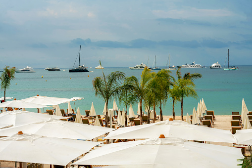 Amazing view on Croisette beach in Cannes and French Riviera with  umbrellas, palm l trees and white sand and motoboats and sailboats in water of bay.   No people( only part of them)