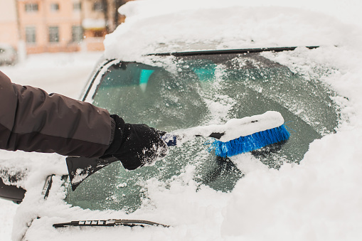 Cleaning car from snow with brush. Car under snow. Winter weather. Climate. Storm. Transportation