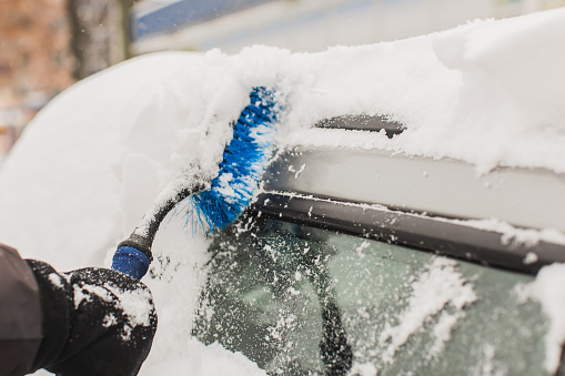 Cleaning car from snow with brush. Car under snow. Winter weather. Climate. Storm. Transportation