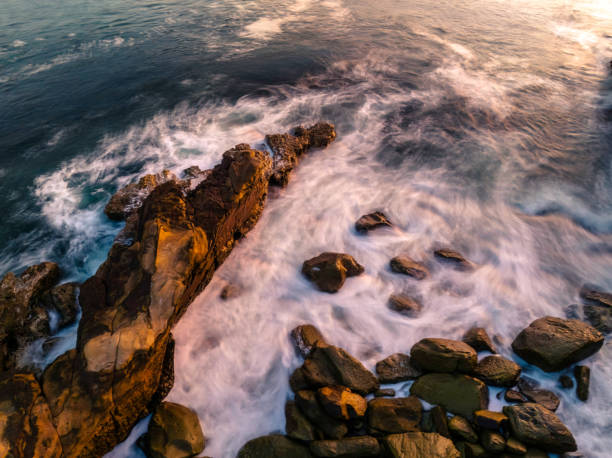 Top down sunrise over the ocean with rocks Aerial sunrise at the seaside with rocks and gentle surf at Avoca Beach on the Central Coast, NSW, Australia. avoca beach photos stock pictures, royalty-free photos & images