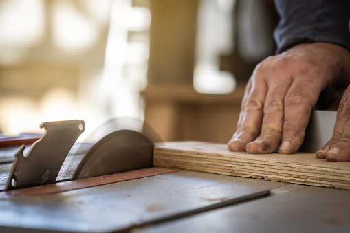 Close-up of a carpenter's hands cutting wood with a circular saw.