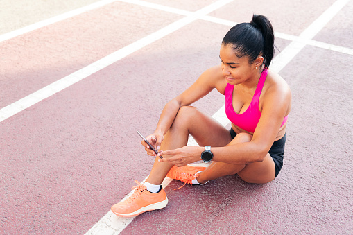 female athlete using her mobile phone sitting on the athletics track after her workout, concept of sport and healthy lifestyle, copy space for text