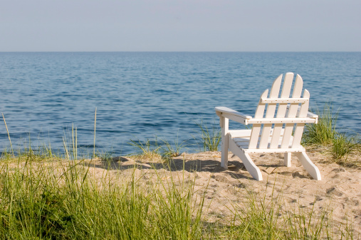 white adirondack chair on a tranquil sand beach overlooking the ocean
