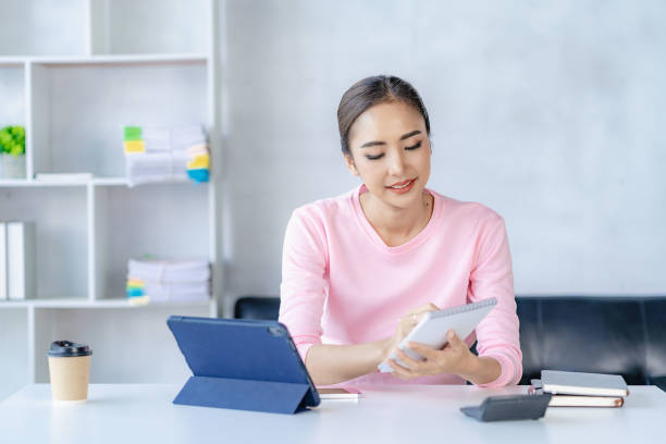 mulher asiática que trabalha on-line com tablet mulher jovem feliz que trabalha em casa - distance running audio - fotografias e filmes do acervo