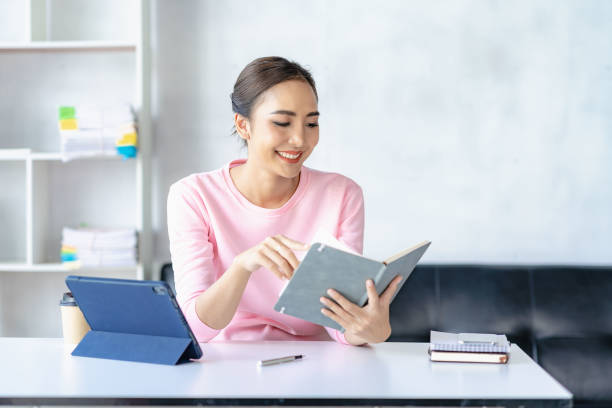 mulher asiática que trabalha on-line com tablet mulher jovem feliz que trabalha em casa - distance running audio - fotografias e filmes do acervo