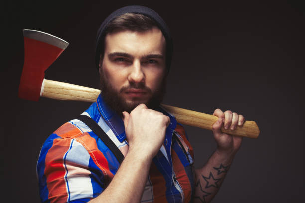 istock Bearded man wearing plaid shirt and balck hat with axe posing over black background in studio 1442888499