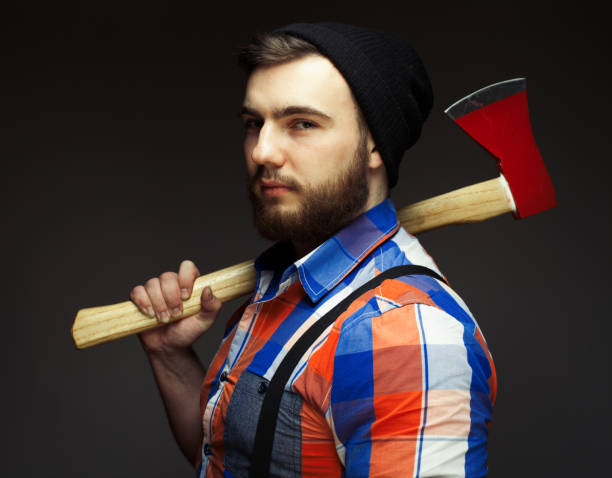 istock Bearded man wearing plaid shirt and balck hat with axe posing over black background in studio 1442888507
