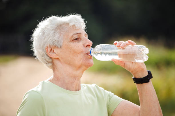 Senior woman drinking water after exercising, summer time, portrait in the park stock photo