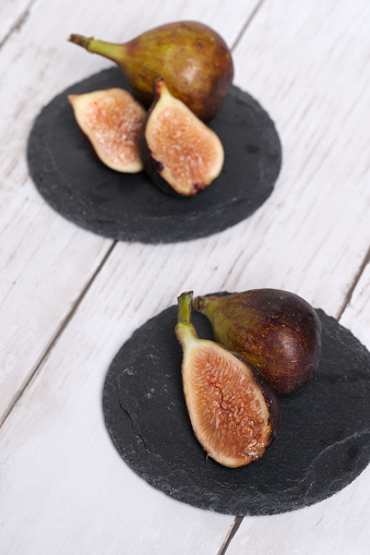 Sliced figs on black slate and isolated on wooden background.