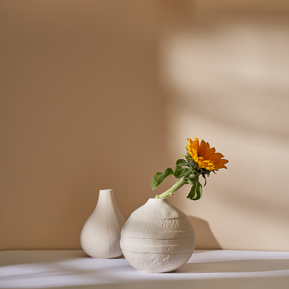 A sunflower in a white ceramic vase against a beige wall