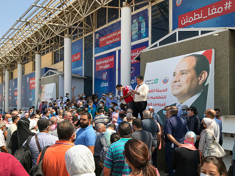 Cairo, Egypt – August 14, 2021: Egyptian citizens at Exhibition land waiting for their turn to receive the Covid-19 coronavirus vaccine, with organizers and background of president