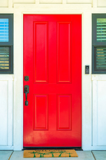 A vertical shot of a red door with a brown welcome doormat