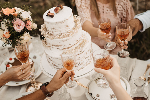 A closeup of the wedding table with cake and people holding glasses with beverages.