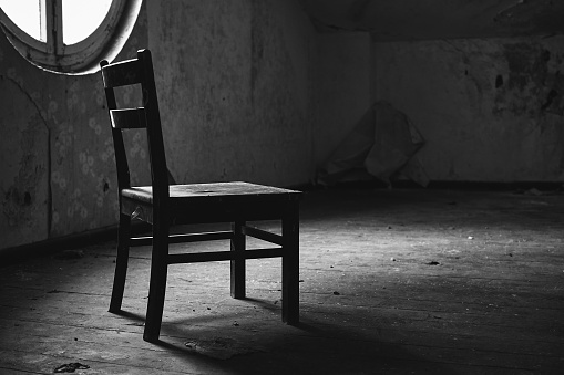 A grayscale of a single chair in an abandoned empty room