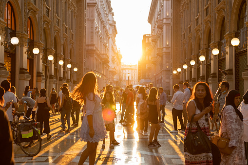 Milano, Italy – September 10, 2021: Galleria Vittorio Emanuele II in the centre of Milan, Italy, with round street lamps on both sides of shopping gallery. Golden sunlight over people