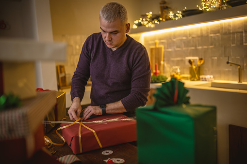 Photo of a young men wrapping Christmas presents at home,