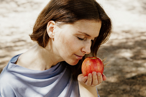 A pretty Spanish woman smelling fresh ripe apple in a garden