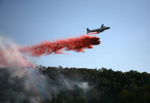 Flying low over a group of firefighters in yellow, a fire fighting plane drops fire retardant on the Snowcreek fire near Highway 285 on July 12, 2022 in a pine forest in the Rocky Mountain foothills of Morrison, Colorado.