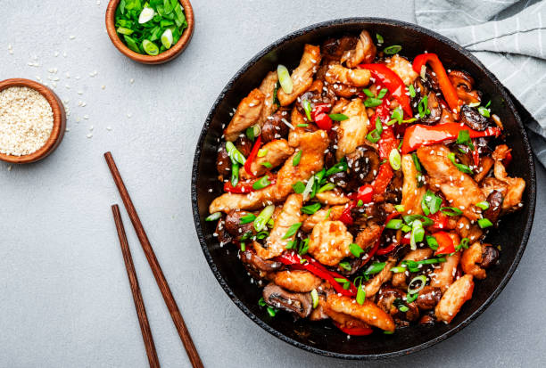Stir fry with chicken, red paprika, mushrooms and chives in frying pan. Asian cuisine dish. Gray kitchen table background, top view, copy space stock photo